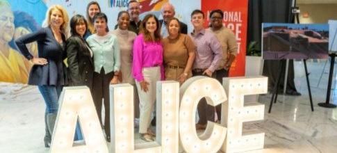 A group of National ALICE Summit 2026 attendees stand and smile behind giant light-up ALICE letters, with a vibrant mural in the background